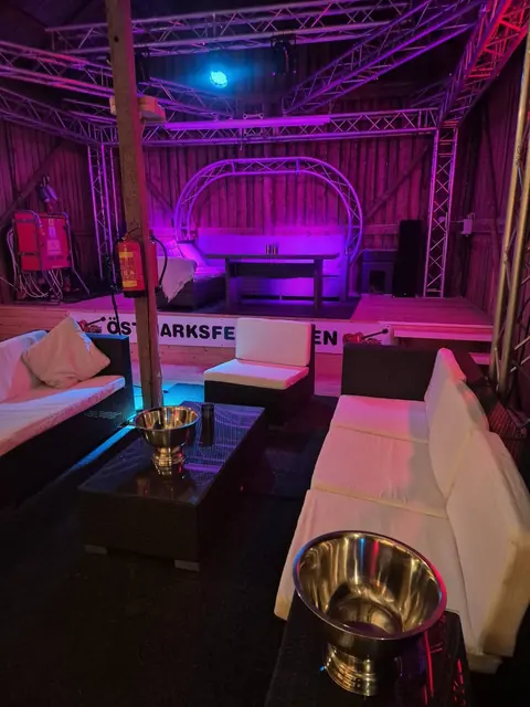 Loungen inne i ladan med vita soffor, champagnehinkar och lila scenbelysning.