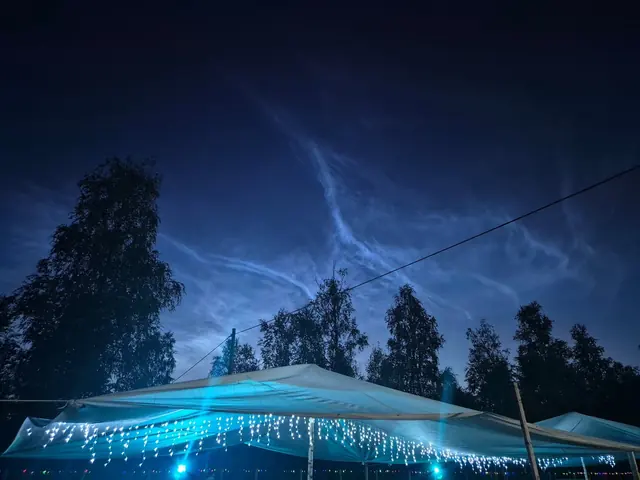 Nattlysande moln på sommarhimlen ovanför de upplysta serveringstälten med ljusslingor.